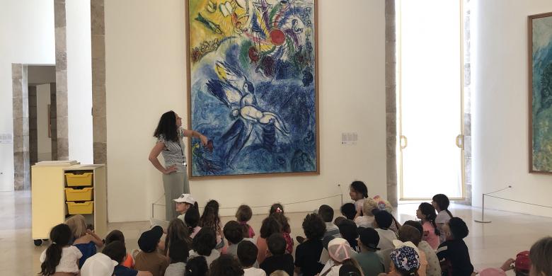 Visite pour enfants par Claudia, guide-conférencière Rmn, devant l'œuvre de Marc Chagall "La Création de l'Homme" (1956-1958), musée national Marc Chagall, Nice © Photo DR / Nice, musées nationaux du XXe siècle des Alpes-Maritimes © ADAGP, Paris, 2022.