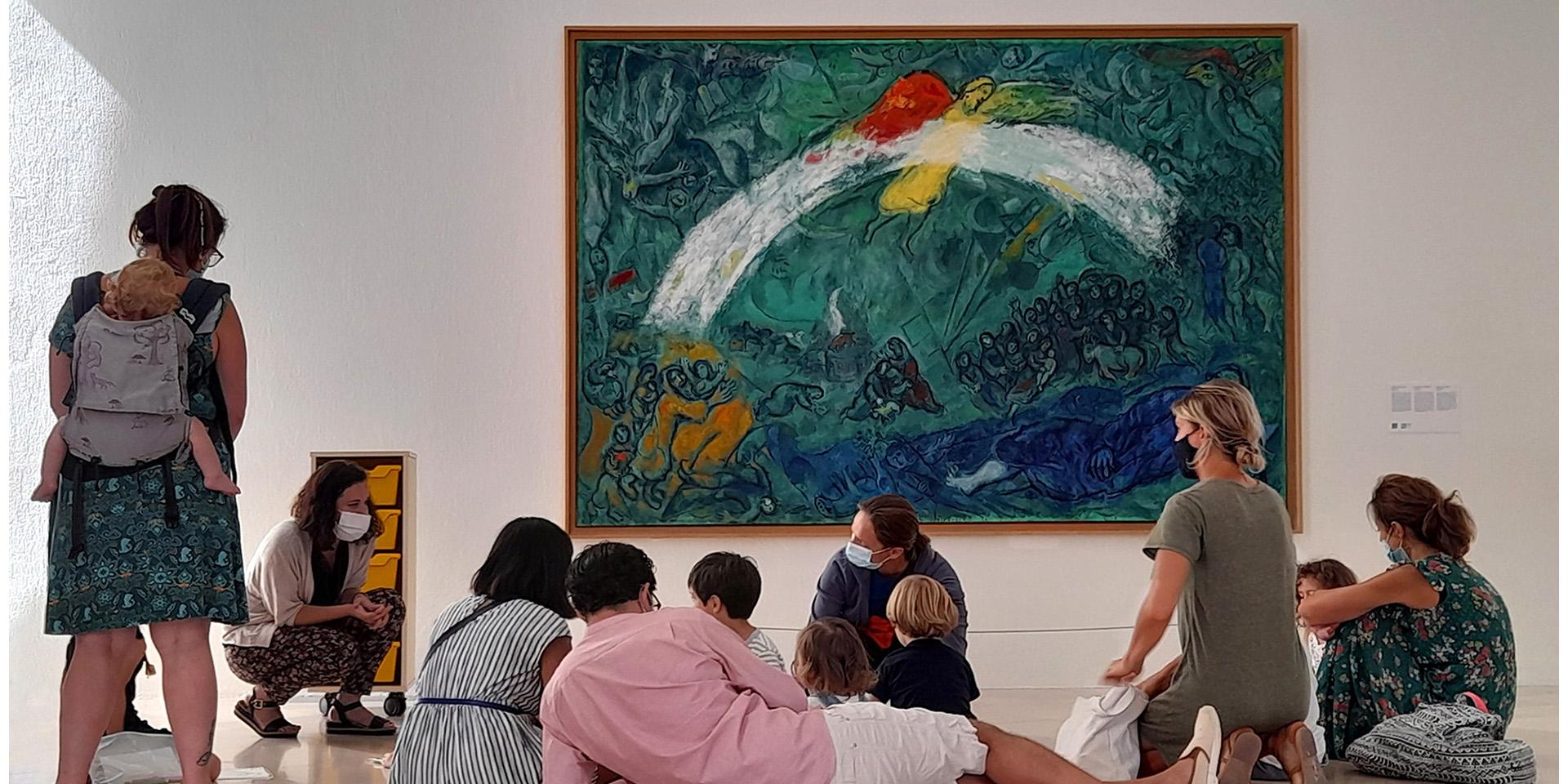 Visite en famille dans la salle du Message Biblique, devant l'œuvre de Marc Chagall, "Noé et l'arc-en-ciel" (1961-1966, huile sur toile). Nice, musée national Marc Chagall. Photo : © DR / musées nationaux du XXe siècle des Alpes-Maritimes © Adagp, Paris, 2021.