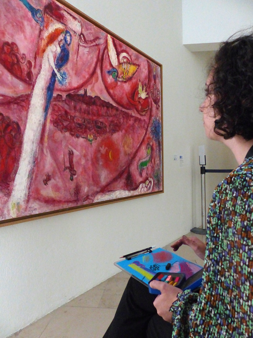 Une femme dessine devant une œuvre du Cantique des Cantiques de Marc Chagall