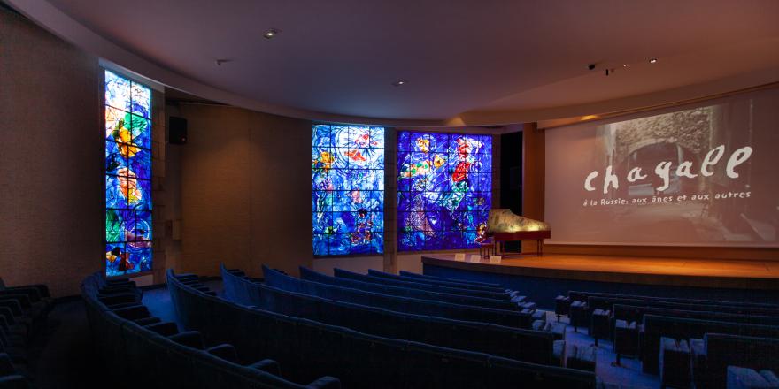 Vue de l'auditorium du musée national Marc Chagall. "La Création du Monde", Marc Chagall, vitrail, 1971-1972. "La rencontre d’Isaac et de Rebecca au puits", couvercle du clavecin peint par Marc Chagall, 1980, musée national Marc Chagall, Nice. Photo : © Gilles Ehrentrant. © ADAGP, Paris, 2020.